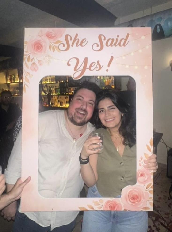 Roger and Rita holding a She Said Yes frame at their engagement party.